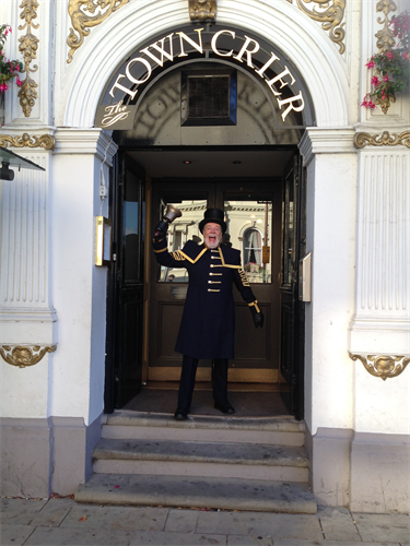 Peter White, Seaford Town Crier standing in front of a building ringing his bell.