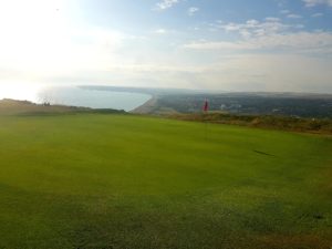 A photograph of the 17th green at the top of Seaford Head with Seaford Bay in the background