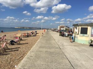 Seaford seafront promeade with Frankie's kiosk and people sunbathing on the beach.