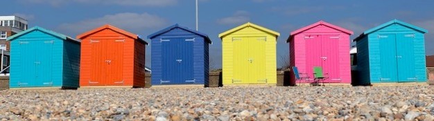 a row of colourful beach huts on a sunny day with blue sky background.