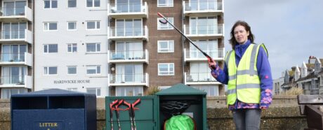 Person holding a litter picking tool, standing next to a bin which has an open door with other litter picking tools inside.