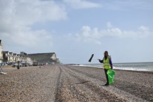 Person on a pebble beach using a litter picking tool with cliff tops in the background.