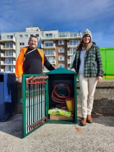 Two people standing beside the SuperBin showing its contents of little picking equipment