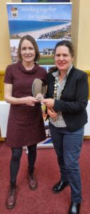 Two people holding a glass award with a banner in the background which read "Working Together for Seaford"