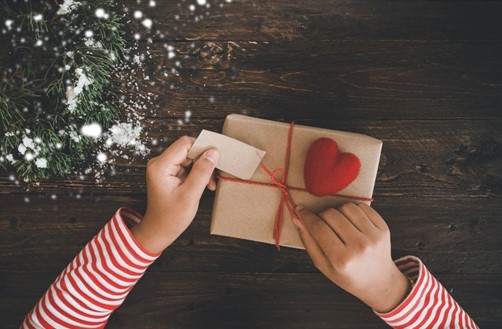 Brown paper present with a red bow and hands attached a tag