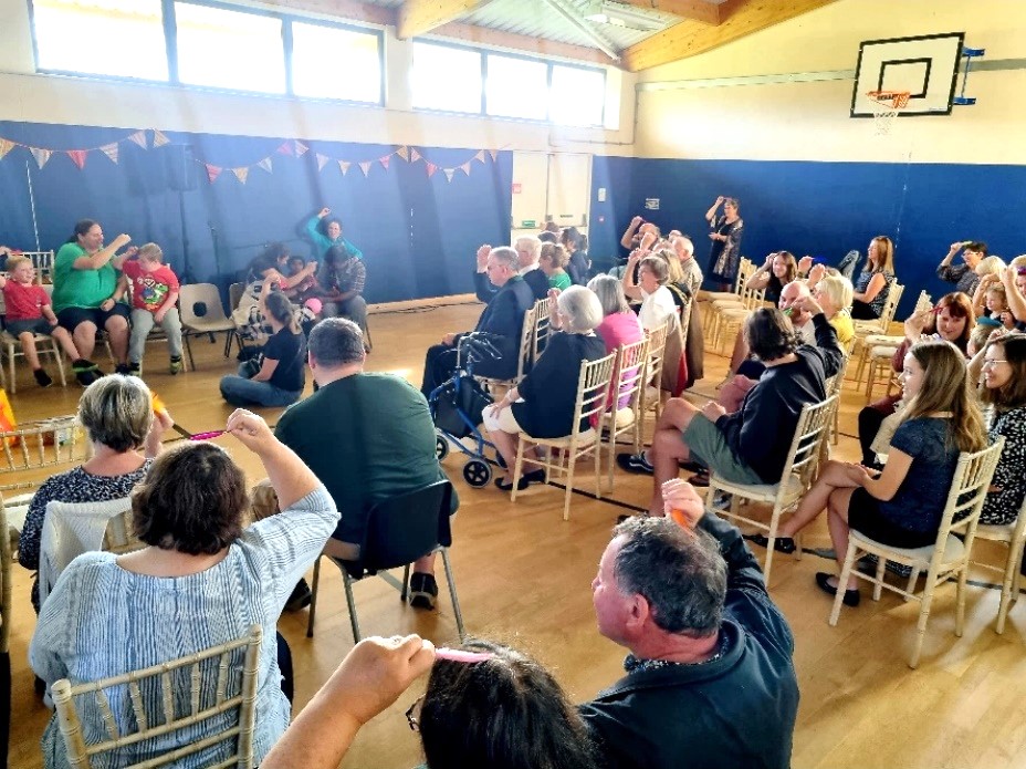 An audience watching and singing holding small coloured feathers on their heads 