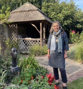 The Mayor of Seaford standing outside in a beautiful garden with a summer house and sculpture.