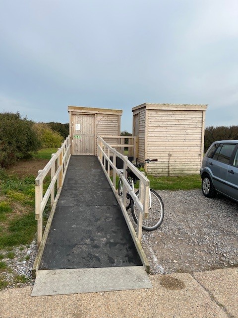 The Compostable Toilet block - a wooden shed-like structure with an ascending accessibility ramp to the toilet door