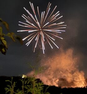 Fireworks high in the sky with bonfire below in the distance