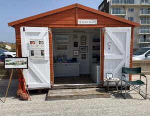 Orange beach hut with the doors wide open showing a selection of photos for sale.